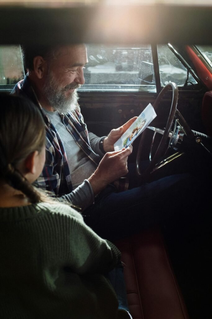 Father reading a greeting card with daughter in a car, depicting family bonding and happiness.