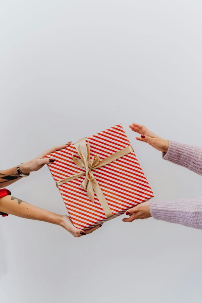 Two people exchanging a beautifully wrapped gift box with red stripes and a gold ribbon.