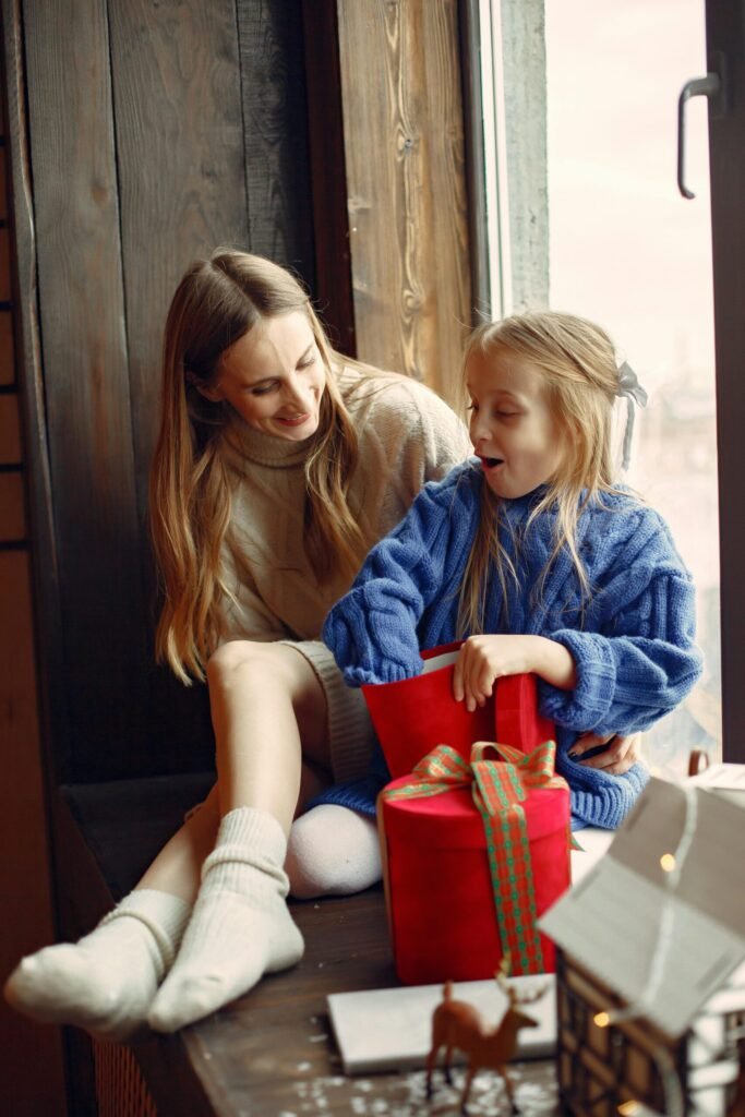 A joyful moment of a mother and daughter opening a Christmas gift by the window.