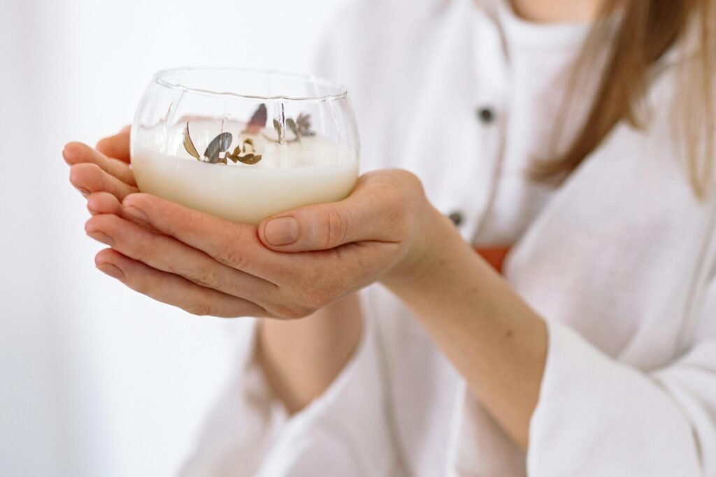 A close-up photo of hands gently holding a decorative candle in a glass holder.
