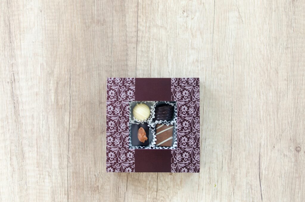 Assorted chocolates in a decorative box placed on a rustic wooden table, viewed from above.