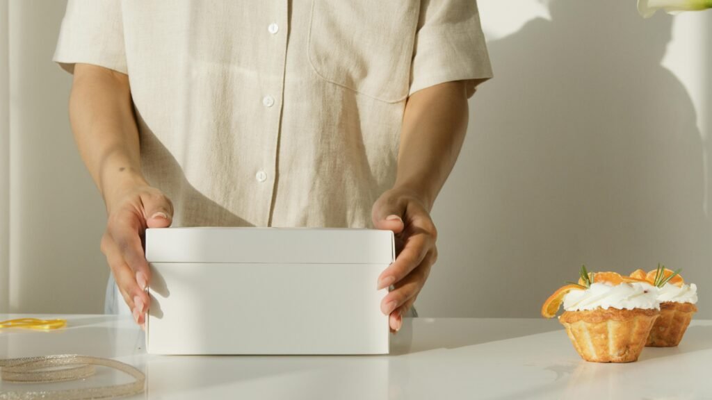 A woman packs cupcakes into a gift box, perfect for celebrations.