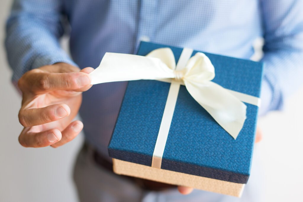 Close-up of man untying bow while opening gift Custom corporate gift boxes in New Zealand. Branded, curated, and delivered nationwide. Perfect for clients, teams, and events.